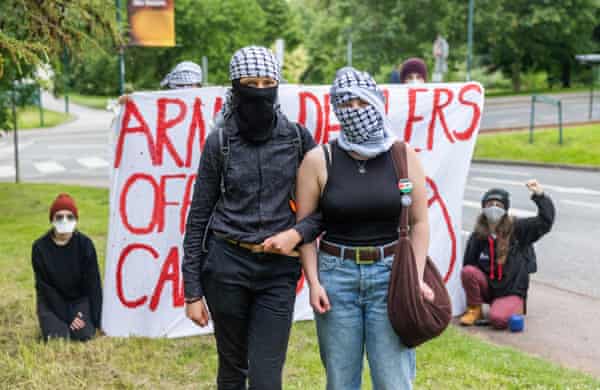 Two women with their faces largely covered stand in front of a large banner